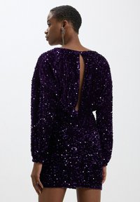 Abito viola con paillettes, dotato di uno scollo profondo sulla schiena, maniche lunghe e una silhouette attillata, caratterizzato da una finitura testurizzata e scintillante.