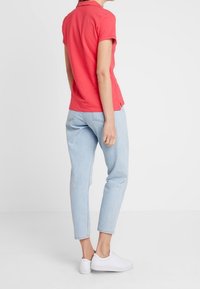 Rotes kurzärmeliges Poloshirt, hellblaue taillierte Jeans und weiße Sneakers. Einfaches Design, glatte Textur und lässige Passform.