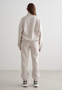 Sudadera gris claro texturizada con cuello alto y ajuste holgado, combinada con pantalones jogger ajustados a juego. Zapatillas negras y blancas.