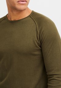 Olijfgroen shirt met lange mouwen gemaakt van gestructureerde stof; heeft raglanmouwen en een ronde hals. Slanke pasvorm met zichtbare stiksels.