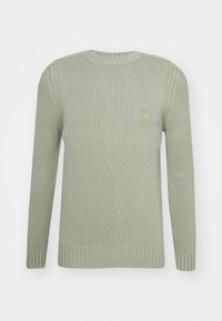 Ljusgrön tröja med ribbad textur, rundad halsringning och långa ärmar. Har en liten, präglad logopatch på bröstet.