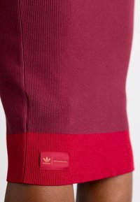 Ribbade stickade kjol i mörkröd och ljusröd, med en enfärgad röd fåll och en broderad Adidas-logotyp i nederkant.