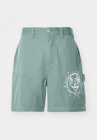 Pantaloni scurți verzi din bumbac, cu o croială lejeră, având două buzunare frontale și un grafic alb al soarelui pe piciorul din dreapta. Hașură simplă, fără modele.