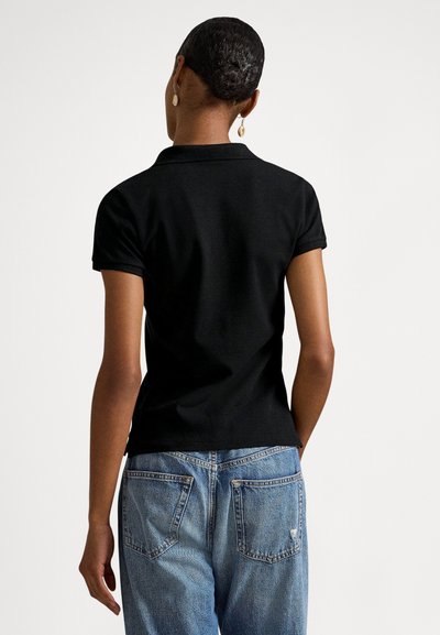 Czarna koszulka polo z krótkimi rękawami, klasycznym kołnierzykiem i dopasowanym krojem, zestawiona z jasnoniebieskimi, postarzanymi dżinsami.