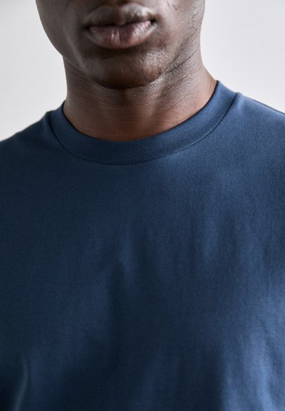 T-shirt en coton bleu marine avec un col rond. Texture douce, tissu lisse et design simple sans motifs ni embellissements.