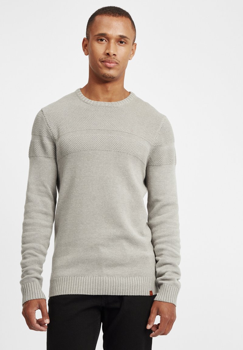 Hellgrauer Strickpullover mit strukturiertem Design, rundem Halsausschnitt sowie gerippten Bündchen und Saum. Wird für einen Kontrast mit schwarzen Hosen getragen.