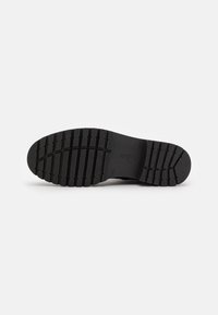 Suola di scarpa in gomma nera con un motivo di battistrada testurizzato. Presenta una forma arrotondata e una finitura liscia con un'impronta del logo su un lato.