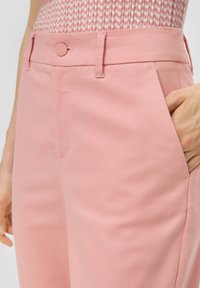 Lichtroze broek gemaakt van een gladde stof, met een knoopsluiting en zijzakken, in een getailleerde pasvorm.