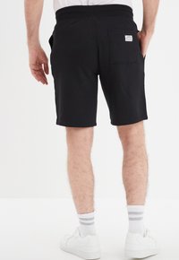 Shorts de algodón negros con un corte relajado, que cuentan con una cinturilla elástica y un bolsillo trasero. Combinados con zapatillas deportivas blancas y calcetines a rayas.
