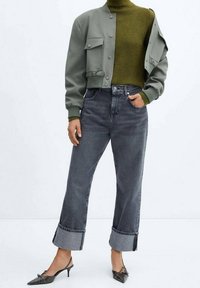 Jean large grise à la coupe courte avec ourlets retroussés, associée à un col roulé vert foncé et une veste bomber gris clair. Chaussures à talons pointus noires.