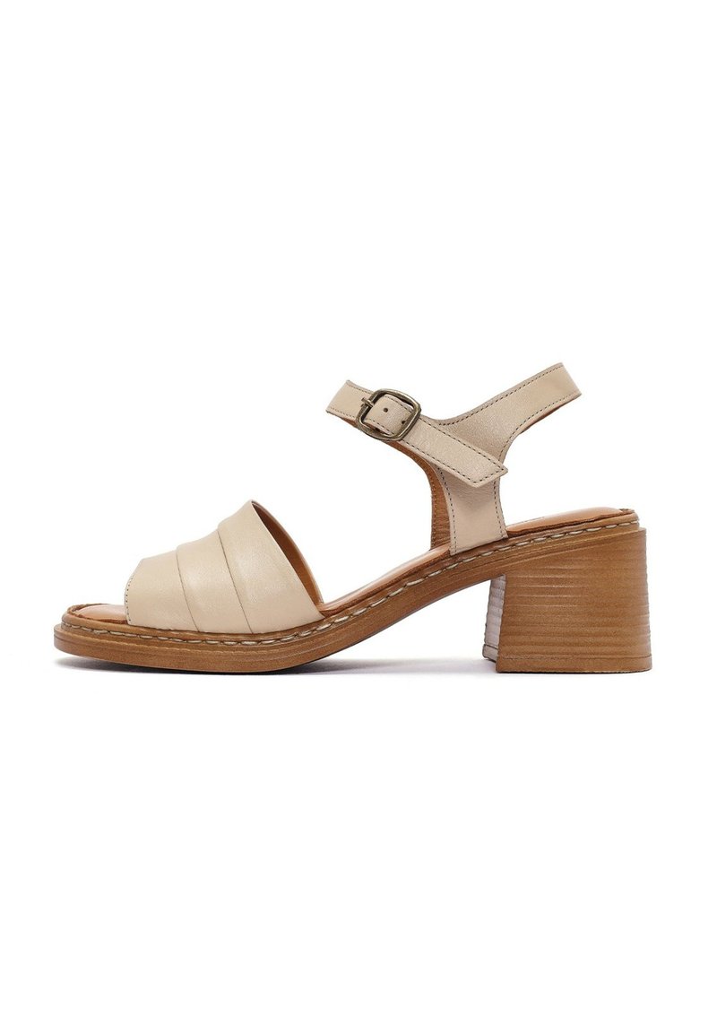 Sandalo in pelle beige con cinturini larghi e chiusura a fibbia. Presenta un tacco in legno e dettagli cuciti sulla suola.