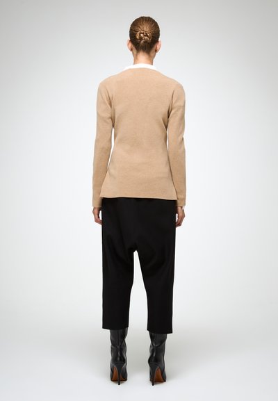 Beige pletený svetr s dlouhými rukávy, zaobleným lemem, kombinovaný s černými volnými kalhotami a černými kozačkami do kolen.