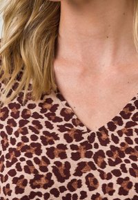 T-shirt en V à imprimé léopard avec une base beige et des taches brunes, fabriqué en tissu doux, offrant une coupe décontractée et une texture lisse.