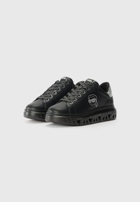 Black sneakers with a smooth leather finish, textured laces, a silver accent at the heel, and a bold patterned sole featuring cutouts.