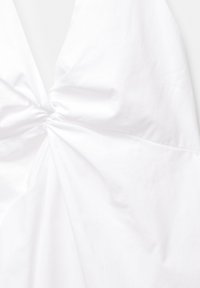 Tessuto di cotone bianco con un dettaglio annodato al centro, caratterizzato da una texture liscia e una caduta fluida che crea pieghe morbide.