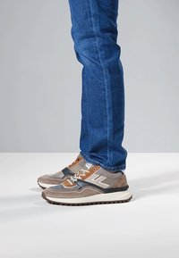 Chaussures de sport beige et gris avec des accents orange, dessus en daim texturé et en maille, dotées d'une semelle blanche épaisse et de détails noirs.