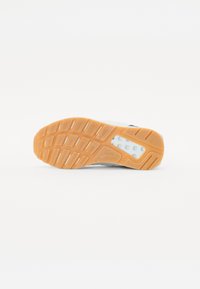 Hvit sneaker med en oransje gummisåle, med et teksturert mønster på sålen og en hvit mellomsåle. Har en liten logodetalj.