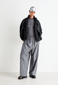 Athletic outfit featuring a black jacket with white stripes, gray fitted shirt, gray wide-leg pants, and black platform shoes.
