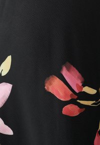 Tessuto nero con un motivo floreale in tonalità di rosa e rosso tenue, caratterizzato da una superficie testurizzata che crea profondità visiva e contrasto.