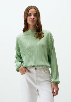 Groene geribbelde trui met een brede halslijn en lange mouwen, gecombineerd met witte broek met hoge taille. Gladde textuur en een relaxte pasvorm.