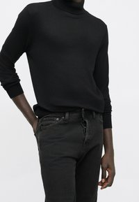 Black turtleneck sweater in a soft knit, paired with dark jeans featuring a five-pocket design and button-fly closure.