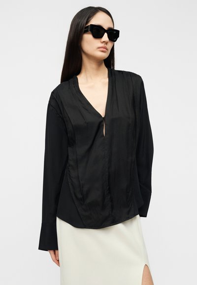 Μπλούζα από μαύρο σατέν με βαθύ ντεκολτέ σε σχήμα V και μακριά μανίκια, με ελαφριά γυαλάδα και πιέτες στα πλαϊνά.