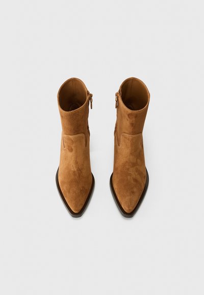 Botine din suede maro, cu vârful ascuțit și fermoar lateral. Textură netedă cu detalii minime, având un toc scăzut tip bloc.