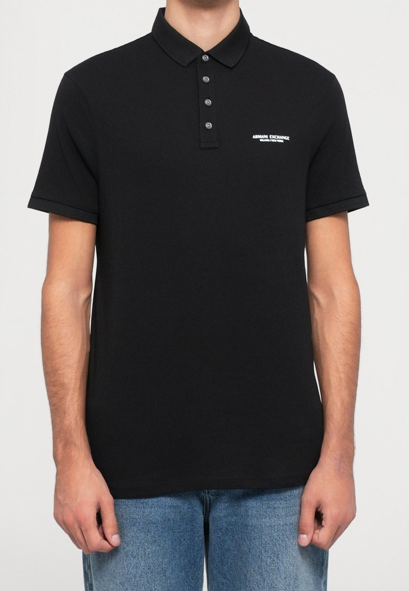 Homme portant un polo manches courtes noir Armani Exchange avec trois boutons et un logo blanc sur la poitrine gauche, associé à un jean bleu.
