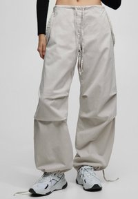 Lichtbeige cargo-broek met elastische boorden, verstelbare taille en zijzakken. Gemaakt van een zachte, gestructureerde stof. Draagt met witte sneakers.