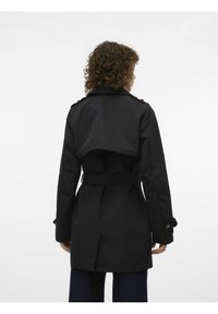 Black trench coat with a belted waist, wide collar, and shoulder epaulets. Features a flowing back design and textured fabric.