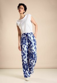 Löst sittande, vit bomullströja med korta ärmar, tillsammans med vida byxor i blå och vit ikatmönster. Elastisk midja, sidofickor.