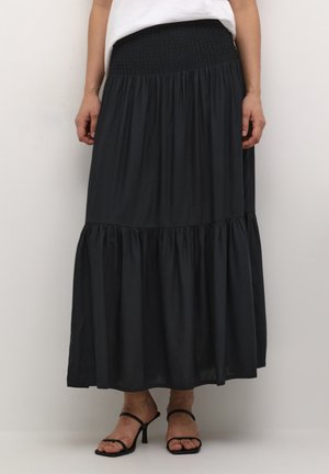 Gonna maxi nera con vita arricciata, caratterizzata da un design a strati e un tessuto morbido e fluido. Abbinata a tacchi neri con strappo.