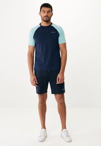 Námorně modré sportovní tričko se světle modrými raglánovými rukávy, spárované s námořnickými šortkami. Tkanina vypadá hladce, úzký design, s logem na tričku.