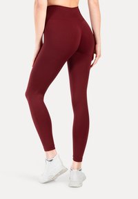 Leggings burdeos de cintura alta con una tela suave, ajuste ceñido y dobladillo limpio, combinados con zapatillas deportivas blancas con una suela texturizada.