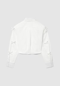 Weißes, langärmeliges, kurzes Hemd mit Kragen und sechs kleinen Schleifen entlang der Rückseite beider Ärmel, auf einem grauen Hintergrund flach ausgelegt.