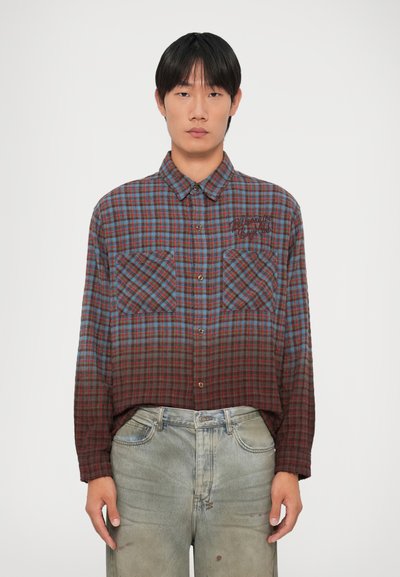 Rode en blauwe geruite shirt met twee borstzakken, ronde kraag en een recht vallende snit. De stof heeft een zachte textuur die geleidelijk donkerder wordt naar de onderkant.