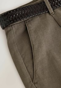 Pantaloni verde oliva con un tessuto texture e tasche a punta, dotati di una cintura in pelle intrecciata marrone scuro in vita.