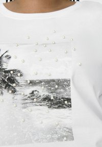 Valkoinen puuvillapaita, jossa on mustavalkoinen merikuvio. Koristeltu ripotelluilla lähdehelmillä tekstuurin ja yksityiskohtien lisäämiseksi.