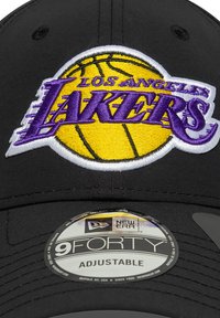 Sort baseball cap med en justerbar rem. Udsmykket med et broderet Los Angeles Lakers-logo i lilla, gul og hvid på forsiden.