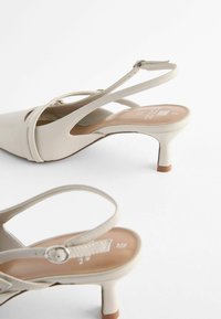 Béžové slingback podpatky s špičatou špičkou a tenkým páskem, s malým podpatkem a hladkou texturou. Dekorace s přezkou na pásku.