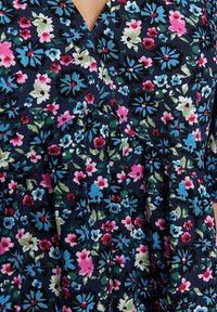 Granatowa sukienka w kwiaty z małymi różowymi, niebieskimi i białymi kwiatami, z teksturowanym materiałem i marszczonym fasonem dla zwiększenia objętości.