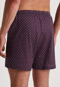 Boxers pour homme en tissu bleu marine foncé avec un petit motif géométrique rouge et blanc. Taille élastique avec une coupe ample.
