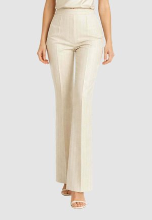 Donna con pantaloni a vita alta color beige a gamba larga con sottili righe verticali e sandali beige con tacco aperti davanti.