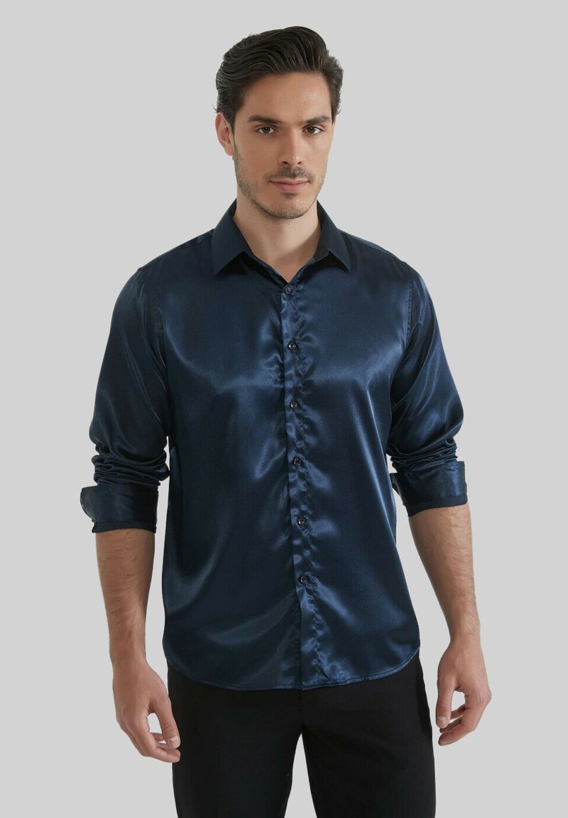 Chemise habillée en satin marine avec un col boutonné, des manches longues et une texture lisse ; dotée de boutons foncés et d'une coupe ajustée.