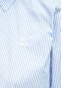 Πουκάμισο με ανοιχτό μπλε ρίγες από απαλό ύφασμα με λευκό κεντημένο λογότυπο "HUGO". Διαθέτει κλασικό γιακά και κούμπωμα με κουμπιά.