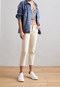 Spijkerjack, cropped zwart-wit gestreepte top, lichtcrème taps toelopende broek, witte sneakers met zwarte accenten, houten vloer als achtergrond.