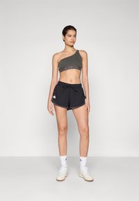 Asymmetrisk mörkgrå ribbad sportcroptop med broderade detaljer, kombinerad med svarta sportshorts med dragsko och sidostrippar.