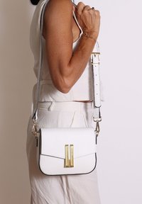 Borsa a tracolla bianca in pelle con chiusura a pattina, dettagli in metallo dorato e tracolla staccabile con bordo grigio chiaro.