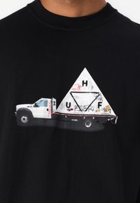 Sort t-shirt med et grafisk motiv af en hvid lastbil med en trekantet, graffiti-dækket last. Accenter omfatter røde striber og mønstre.