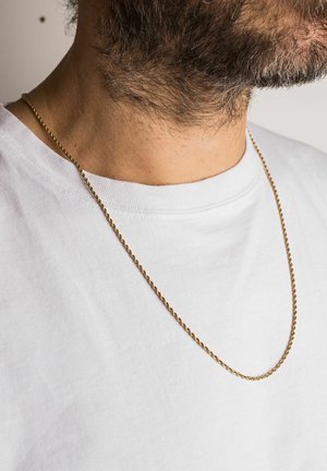 Colier din lanț împletit de culoare aurie purtat peste un tricou alb, evidențiind textura sa netedă și suprafața reflectorizantă în contrast cu pielea.